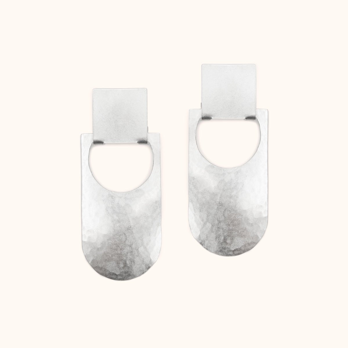 An elongated curved earring with a circular cut out that hangs from a square stud earring. Made in solid sterling silver and finished with a hammered texture. The Botao Earrings are designed and handcrafted in Portland, Oregon.