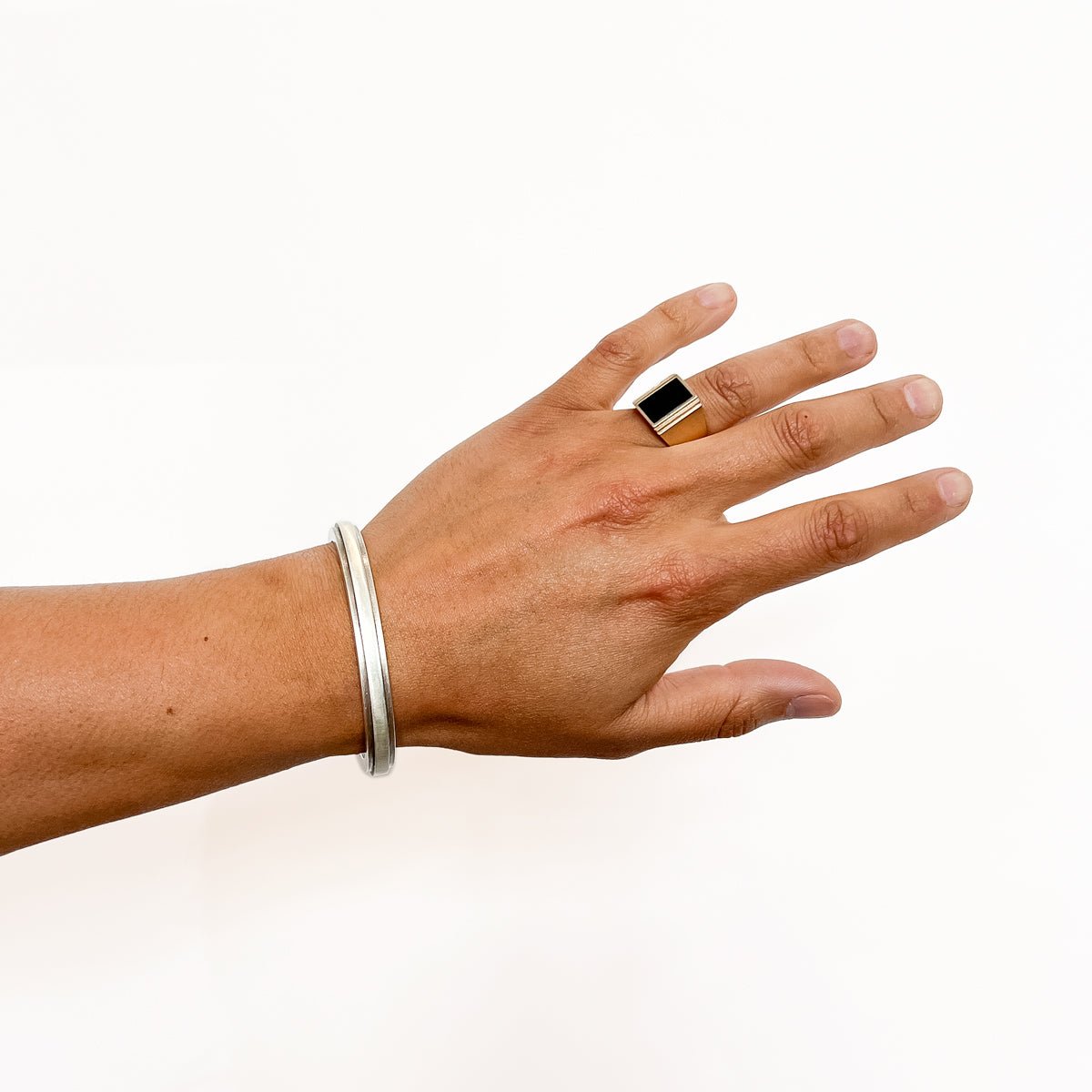 A model wears a wide band signet ring with a rectangle of Oregon Black Jasper Inlay flanked by a stair step cut out design. Made in bronze. Designed and handcrafted in Portland, Oregon.