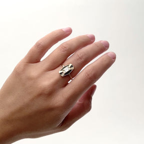 An angular 14k gold ring with a single lab grown baguette diamond in a north/south position in the center. Flanking the diamond are four panels of Oregon black jasper, between gold etchings. The model rotates their hand from side to side as the ring sits flatly on the middle finger. The Imber ring is designed and handcrafted in Portland, Oregon.