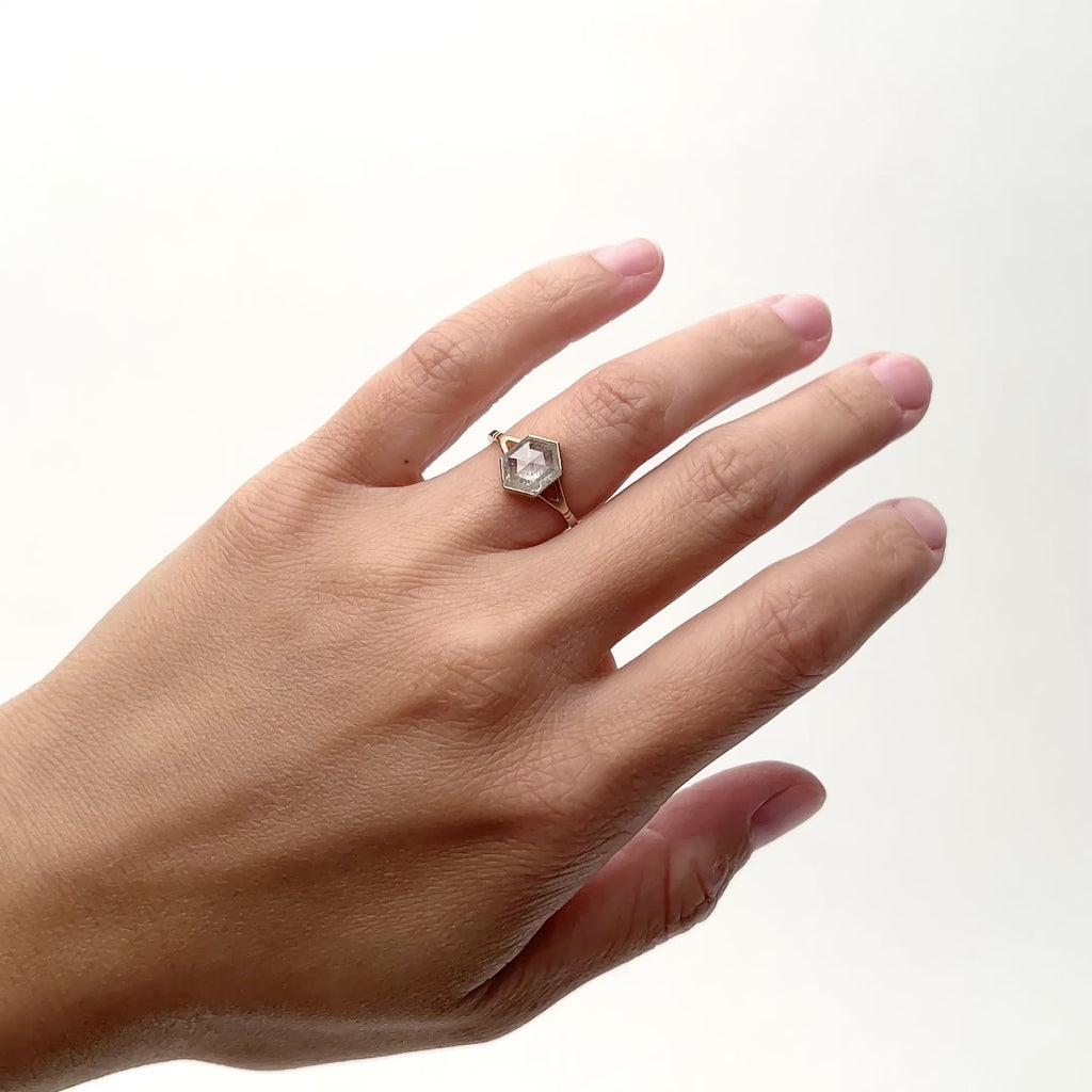 A model wears a hexagon shaped salt and pepper diamond set in a 14k gold band. The band features a Y shaped shank with two detached lines on either side. Designed and handcrafted by in Portland, Oregon. 