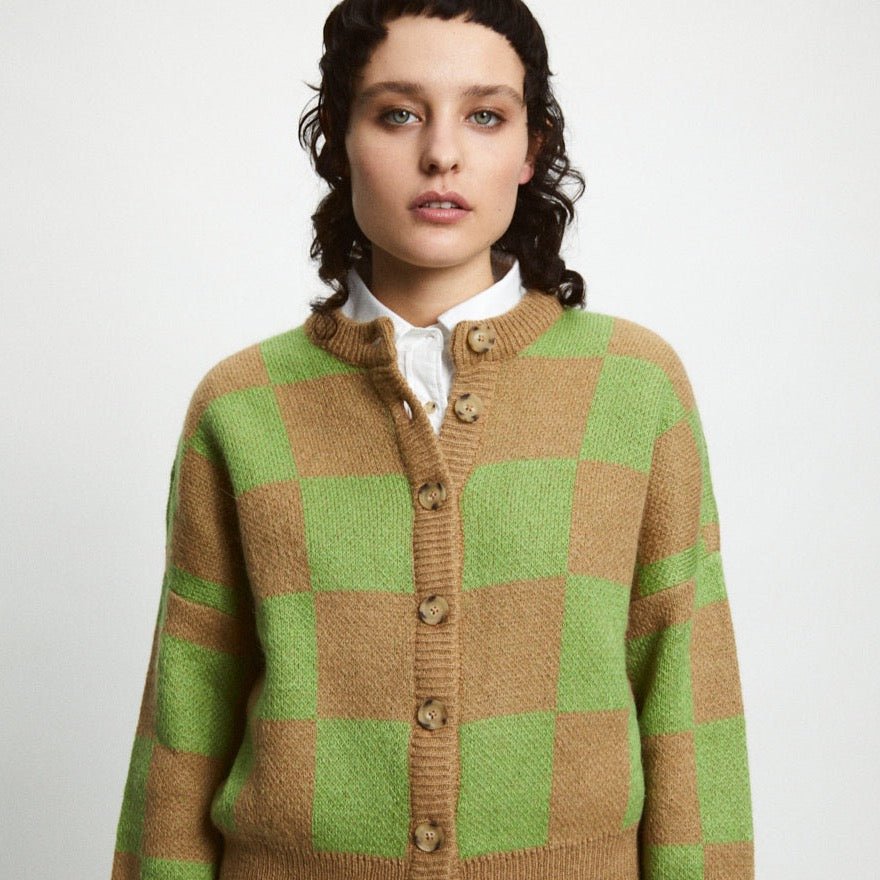 A model wears a knitted button up cardigan in a brown and green checkerboard pattern. The Ellen Sweater is designed by Rita Row and made in Girona, Spain.