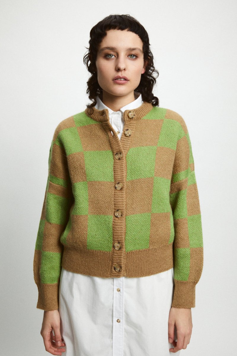 A model wears a knitted button up cardigan in a brown and green checkerboard pattern. The Ellen Sweater is designed by Rita Row and made in Girona, Spain.