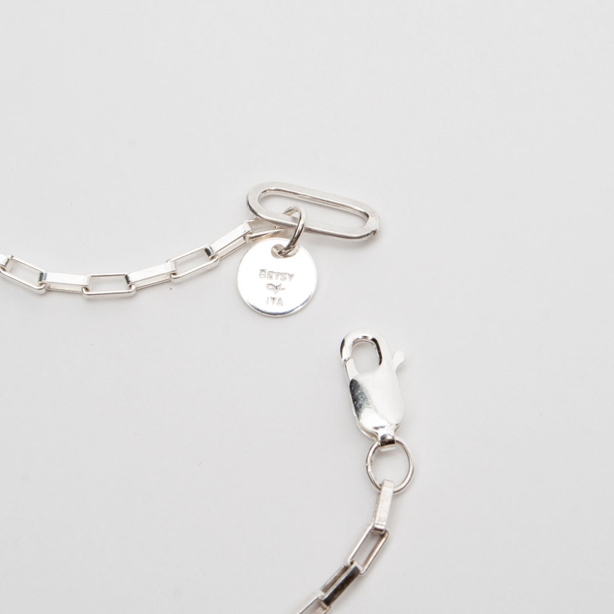 Photo shows a sterling silver lobster claw clasp at the end of a small link chain necklace. The clasp portion of the necklace features a Betsy & Iya tag. Designed and handcrafted in Portland, Oregon.