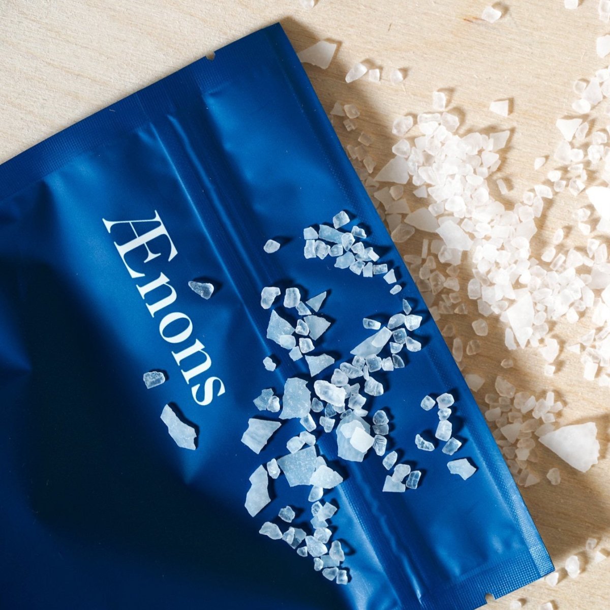 A bright blue open package spills out mineral bath salts. The After Hours Mineral Bath Soak with Lavender + Jasmine Extracts is crafted by Aenons and made in Los Angeles, CA.