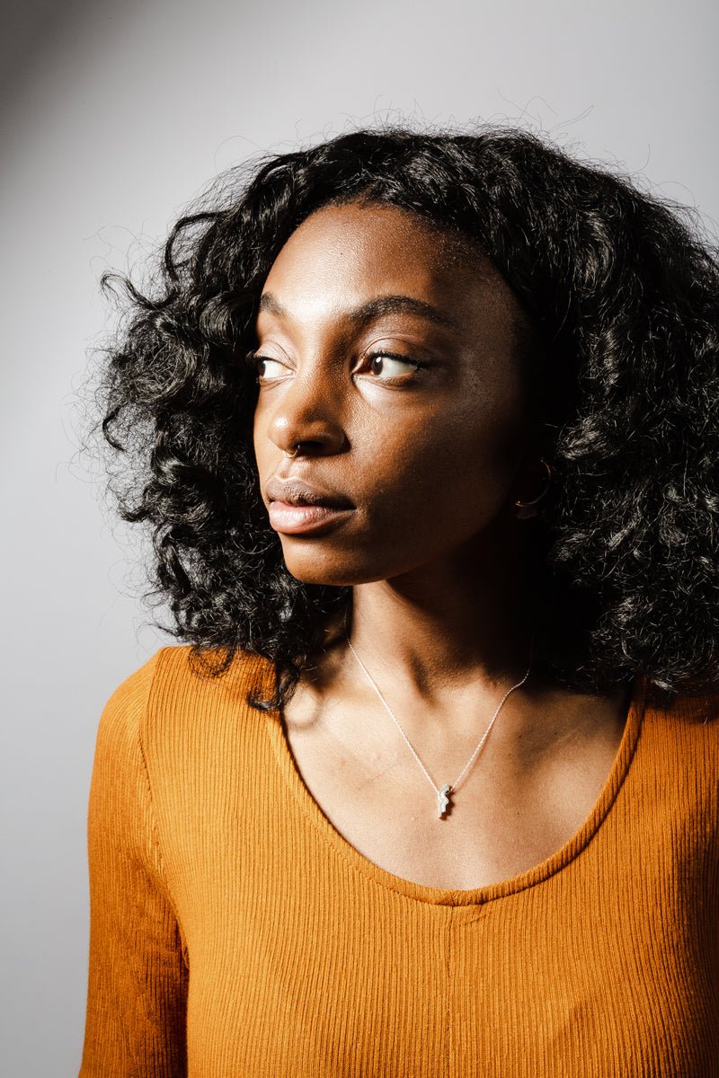 The sterling silver betsy & iya Amare necklace, styled on a model with an ochre dress.