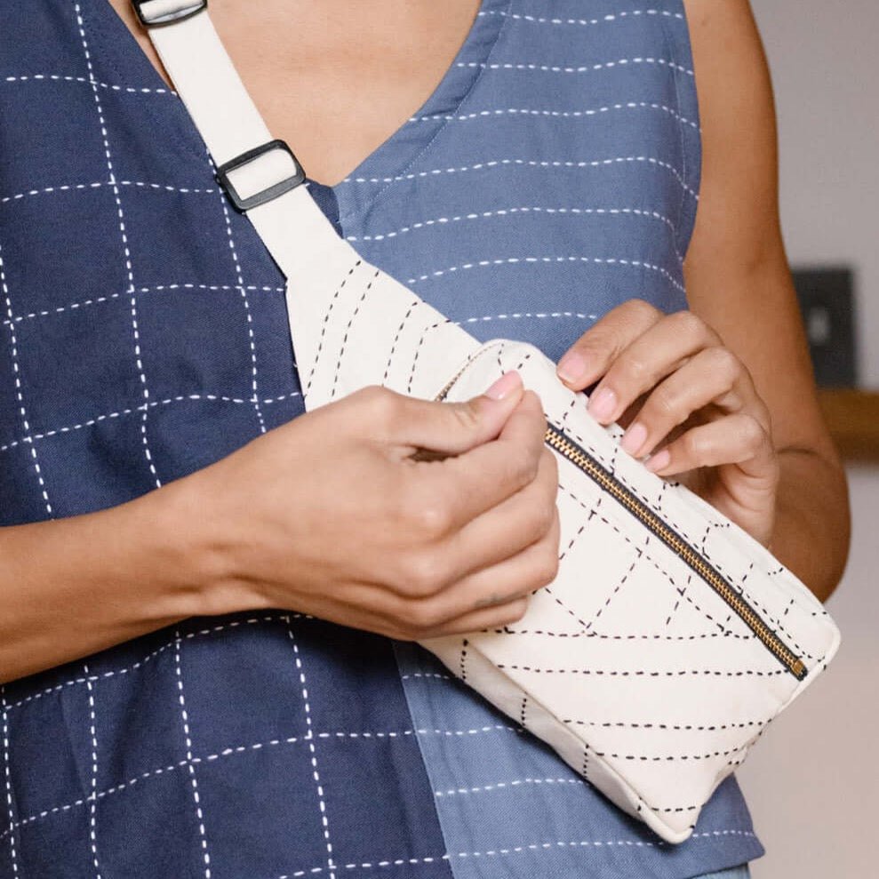 A model wears an off white crossbody bag with black stitching. The Crossbody Belt Bag in Bone is designed by Anchal in Louisville, KY and handmade in Ajmer, India.
