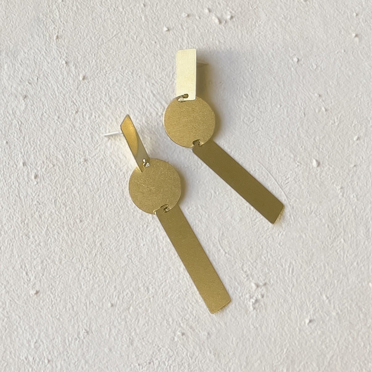 A long brass earring made with two rectangular pieces interconnected with a single circular shape. Designed and handcrafted in Portland, Oregon.