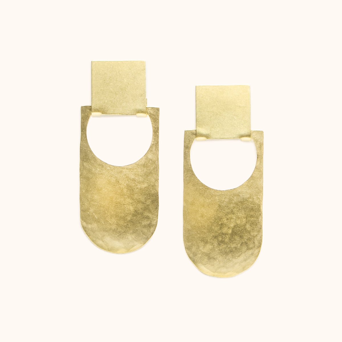 An elongated curved earring with a circular cut out that hangs from a square stud earring. Made in brass and finished with a hammered texture. The Botao Earrings are designed and handcrafted in Portland, Oregon.