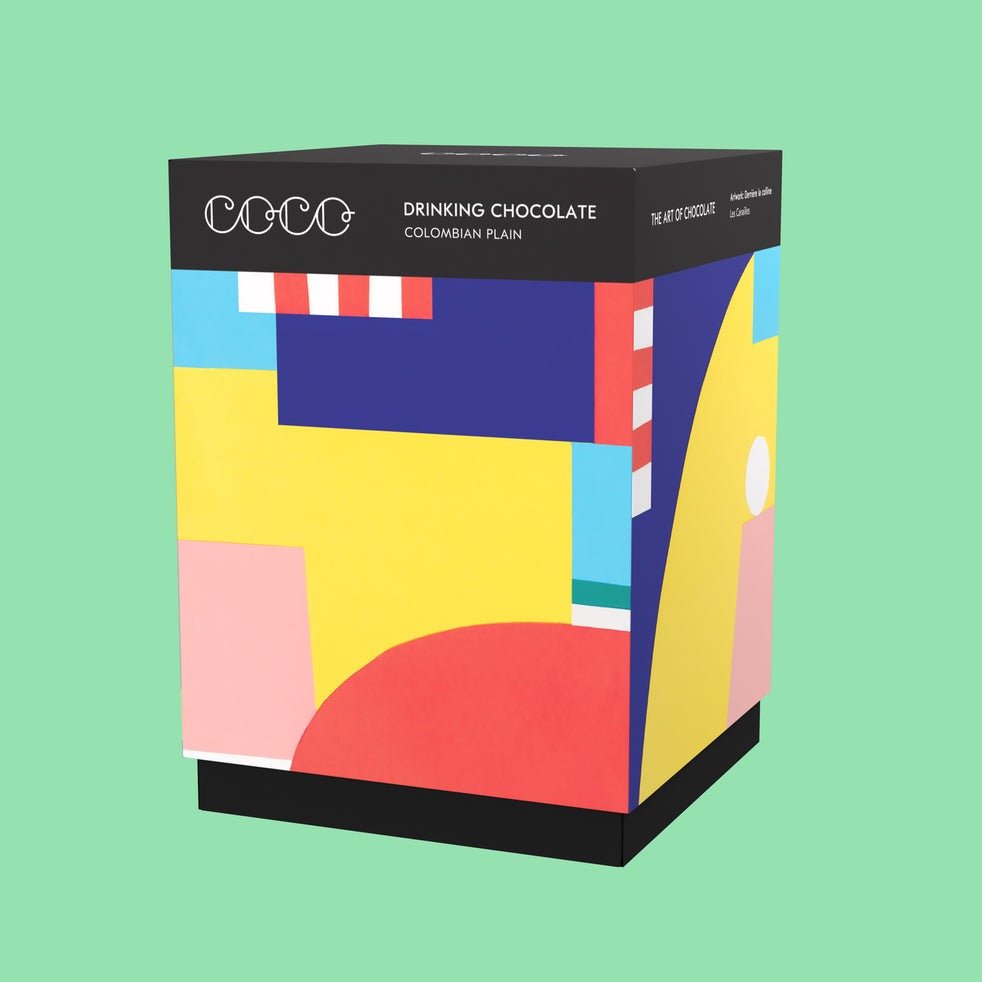 A multicolored square box holds a powdered cocoa mix. The Colombian Plain Drinking Chocolate is from COCO Chocolatier.
