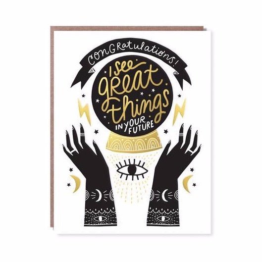 Front of card reads: "CONGRATULATIONS! I SEE GREAT THINGS IN YOUR FUTURE." White, black and gold card with two hands reaching up towards a crystal ball. A single eye is centered with crescents, stars and lightning bolts on the edges. Designed by Hello! Lucky and made in San Francisco, CA. Measures 4.25 x 5.5 inches.
