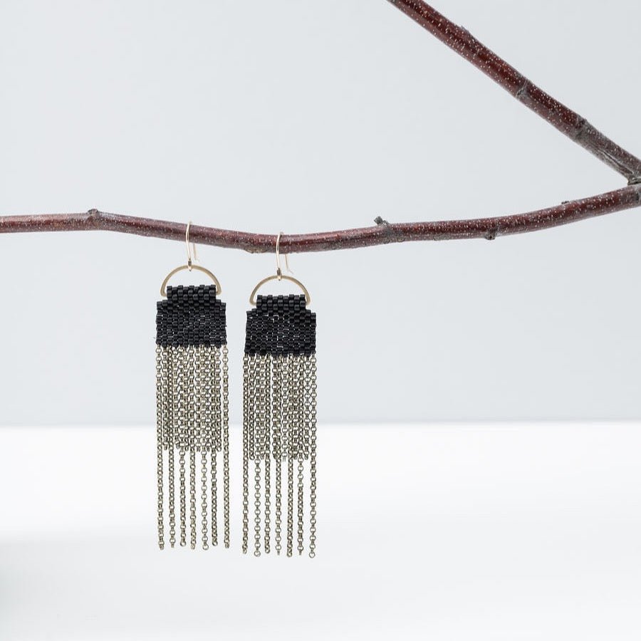 A pair of  black beaded earrings with long strands of antique brass chain secured around a small brass hoop. The Curtain Earrings in Black are designed and handcrafted by A Nod to Design in Portland, OR.