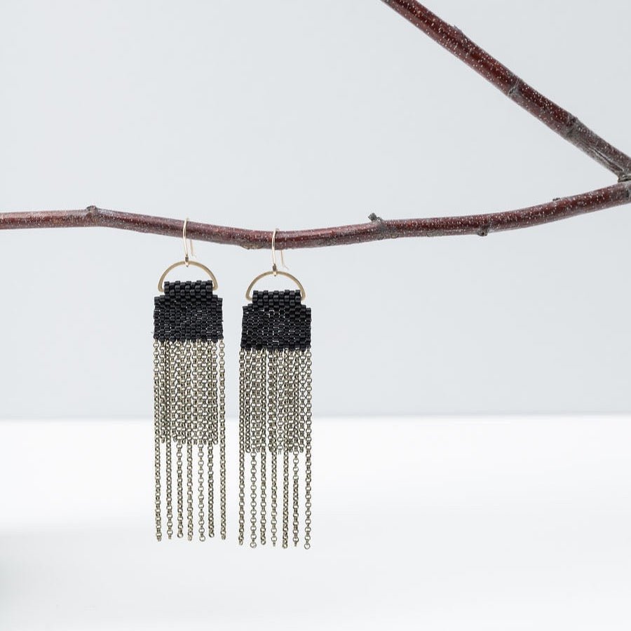 A pair of black beaded earrings with long strands of antique brass chain secured around a small brass hoop. The Curtain Earrings in Black are designed and handcrafted by A Nod to Design in Portland, OR.