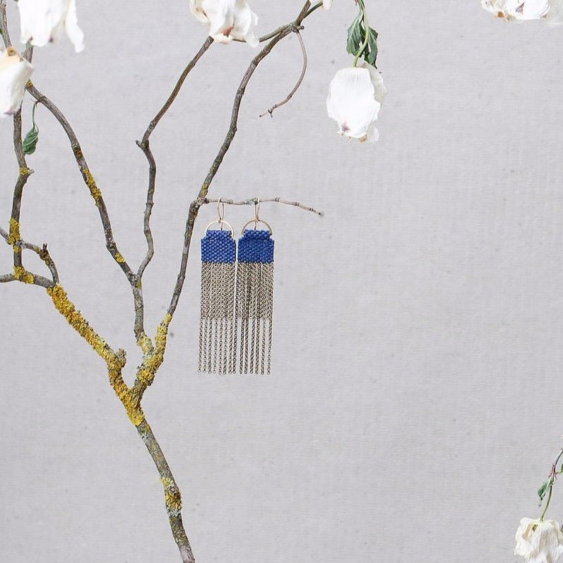 A pair of navy blue beaded earrings with long strands of antique brass chain secured around a small brass hoop. The Curtain Earrings in Navy are designed and handcrafted by A Nod to Design in Portland, OR.