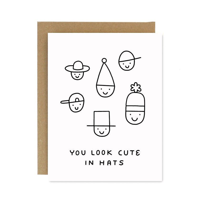 A white card with illustrations of faces wearing different styles of hats. Front of card reads: "YOU LOOK CUTE IN HATS." Designed and handcrafted by Worthwhile Paper in Ypsilanti, MI.