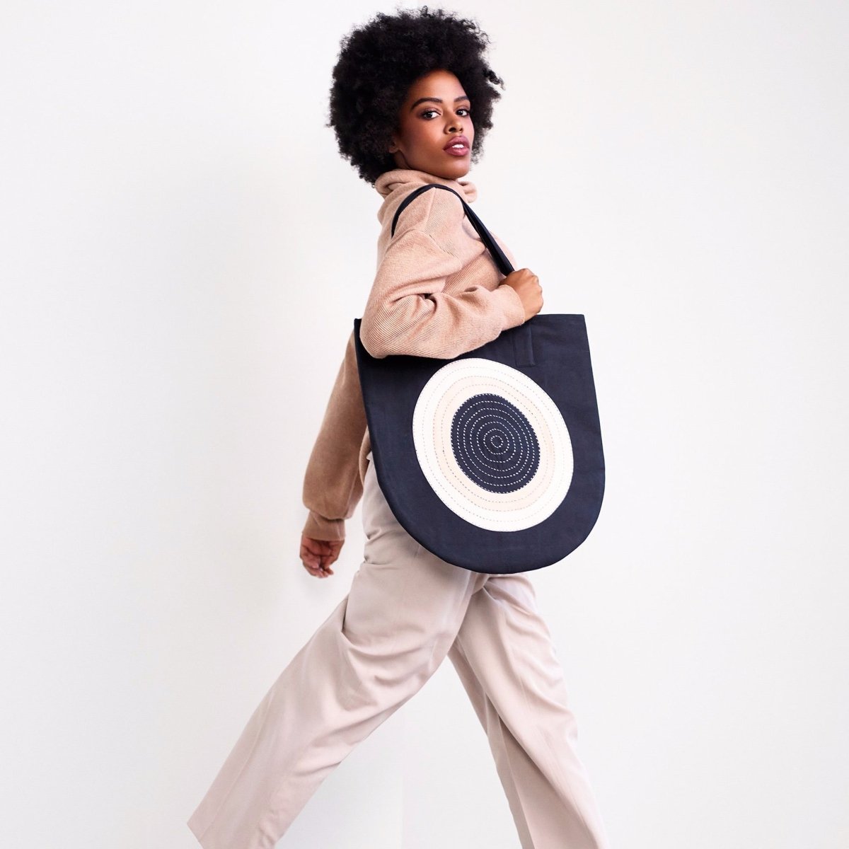 Model holds black tote with cross-stitched circular pattern. Designed by Anchal and handmade in Ajmer, India.