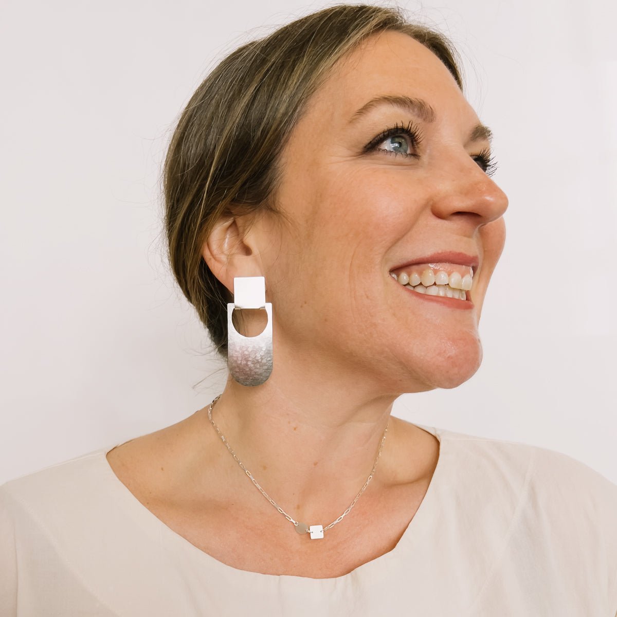 A model wears a short small link sterling silver chain necklace featuring a flat circular and flat square focal piece. Designed and handcrafted in Portland, Oregon.