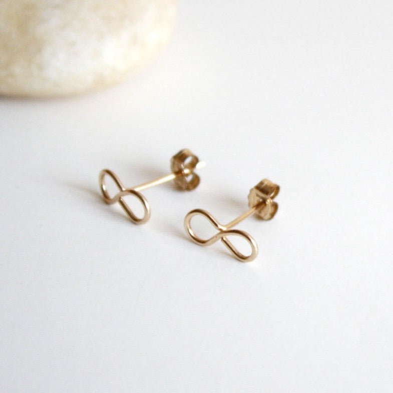A gold tone stud earring in the infinity symbol. The Infinity Stud Earring is designed by Hooks and Luxe and handcrafted in Jackson Heights, NY.