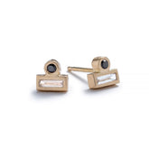 Tiny stud earrings of 14k yellow gold, featuring a small, round, black diamond set against the long side of a white diamond baguette. Hand-crafted in Portland, Oregon.