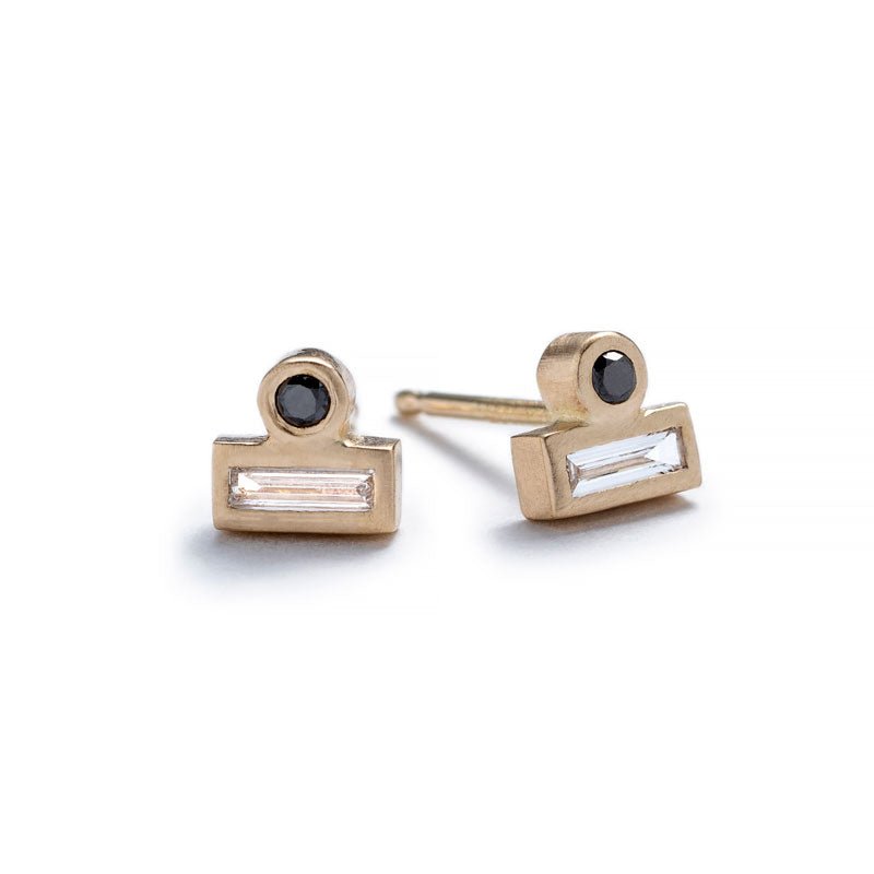 Tiny stud earrings of 14k yellow gold, featuring a small, round, black diamond set against the long side of a white diamond baguette. Hand-crafted in Portland, Oregon. 