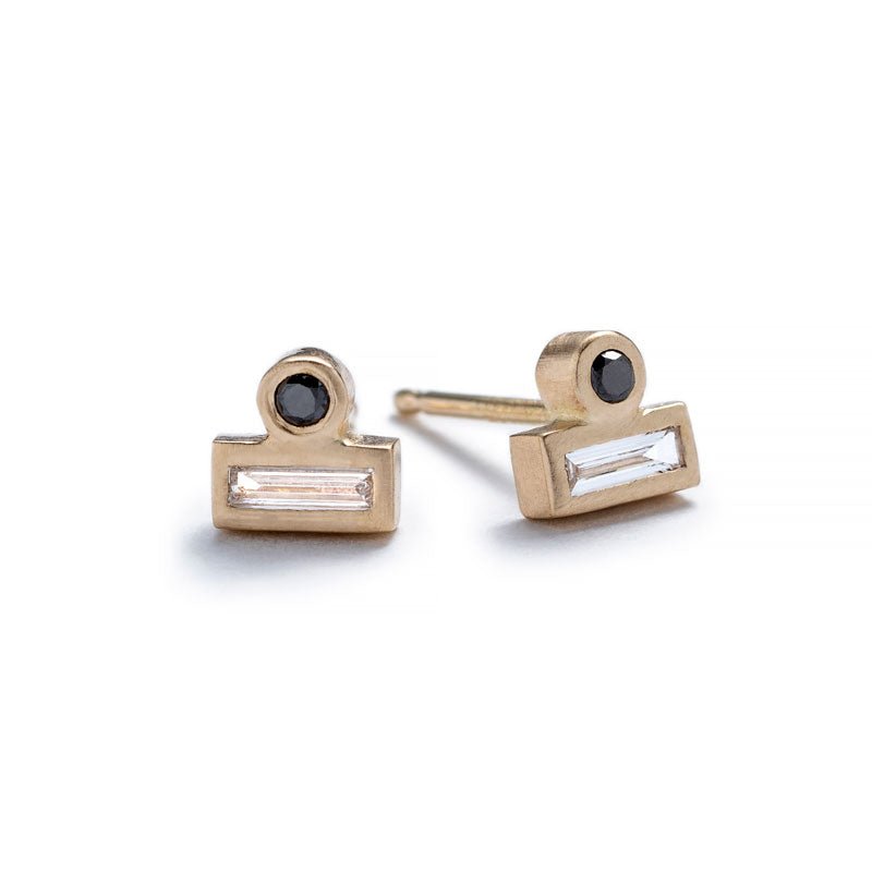 Tiny stud earrings of 14k yellow gold, featuring a small, round, black diamond set against the long side of a white diamond baguette. Hand-crafted in Portland, Oregon.