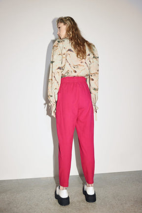 A model shows the back side of a straight leg pant in a bright pink color with an elastic waistband. The Izmir Pants in Fuchsia is designed by Eve Gravel and made in Montreal, Canada.