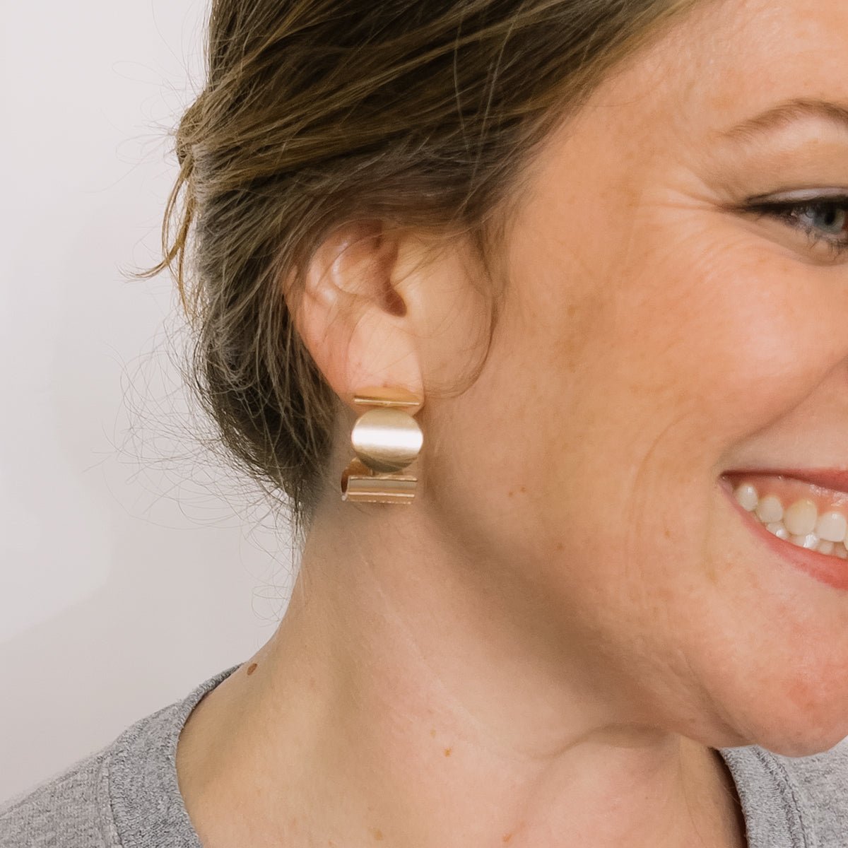 A model wears a wide band bronze hoop earring featuring a circular and rectangular pattern. Designed and handcrafted in Portland, Oregon.