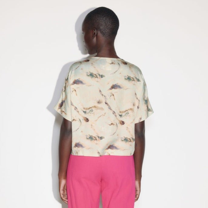 A model shows the back side of a loose fitting top with a boat neck and a brown, green, and blu swirling design. Designed and made by Eve Gravel in Montreal, Canada.