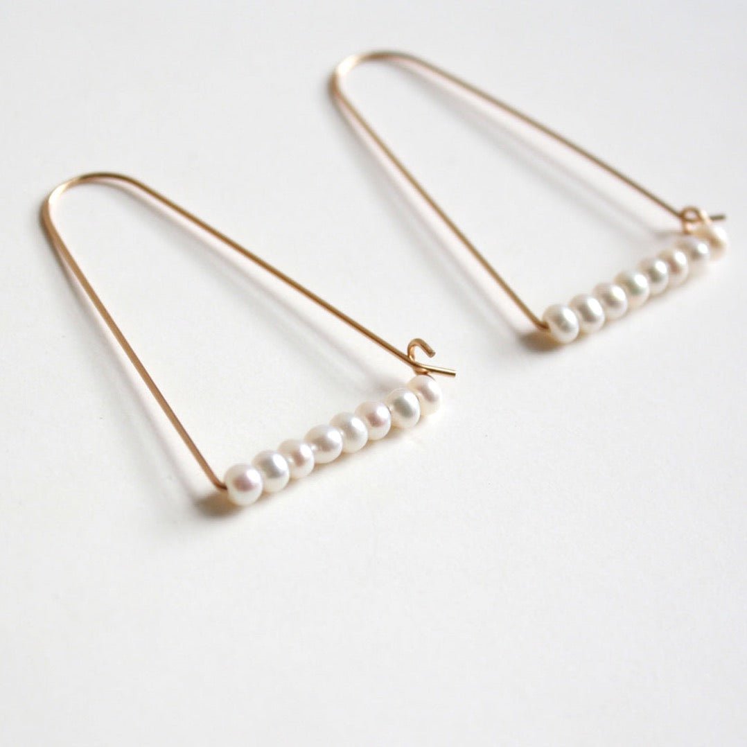 A wide gold tone arch shaped earring with a bar of freshwater pearls at the bottom. The Large Mountain Hoop earrings with Freshwater Pearls are designed by Hooks and Luxe handcrafted in Jackson Heights, NY.