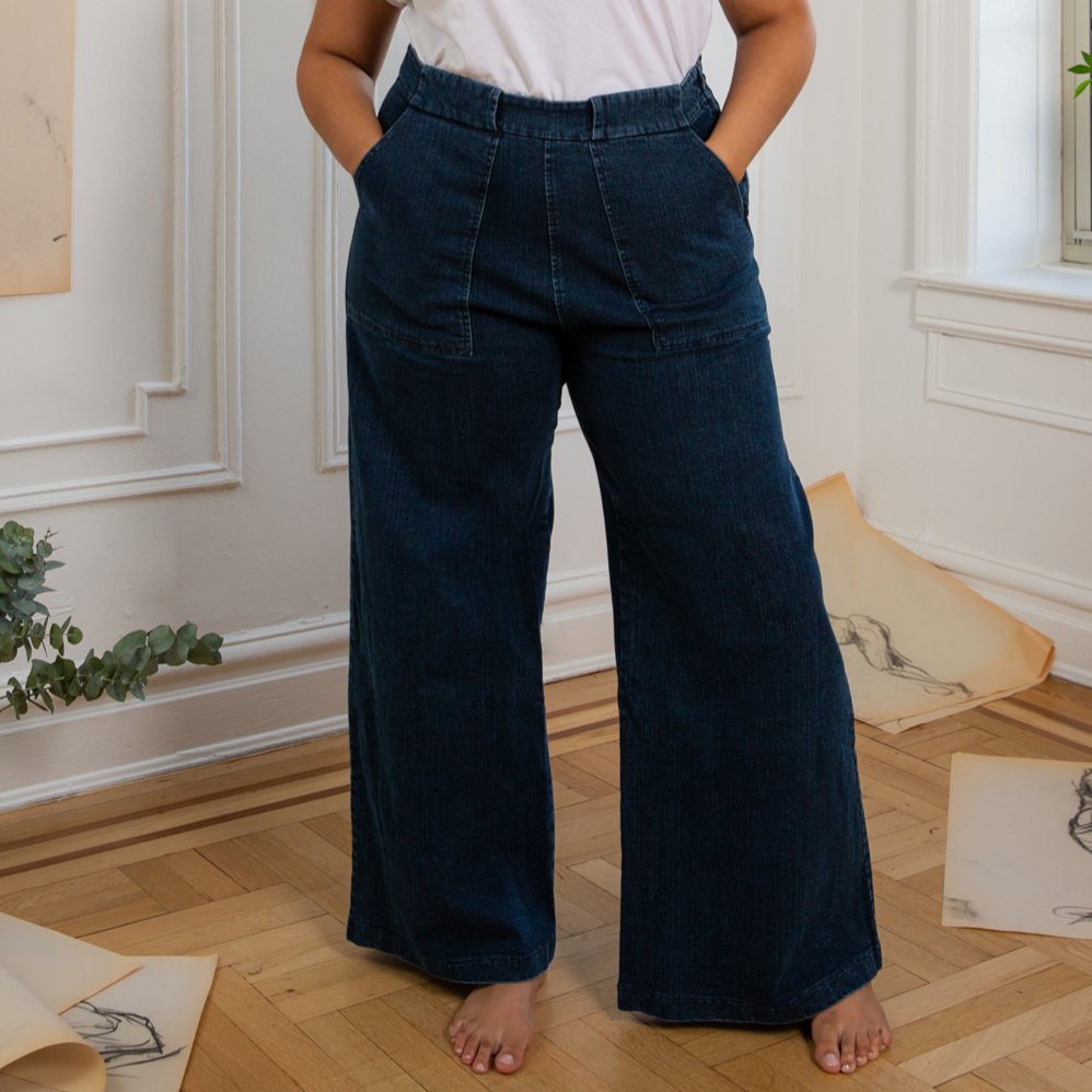 A model wears long wide legged denim pants with large front pockets. The Long Sabrina Jeans in Dark Indigo are designed by Loup and made in New York City, USA.