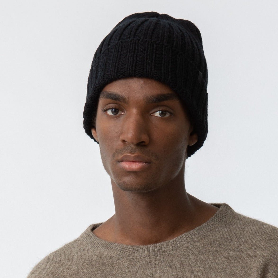 A black cuffed hat with thick ribbed design and decrease detail at the top. The Merino Thick Rib Hat in Black is designed by Dinadi and hand knitted in Kathmandu, Nepal.