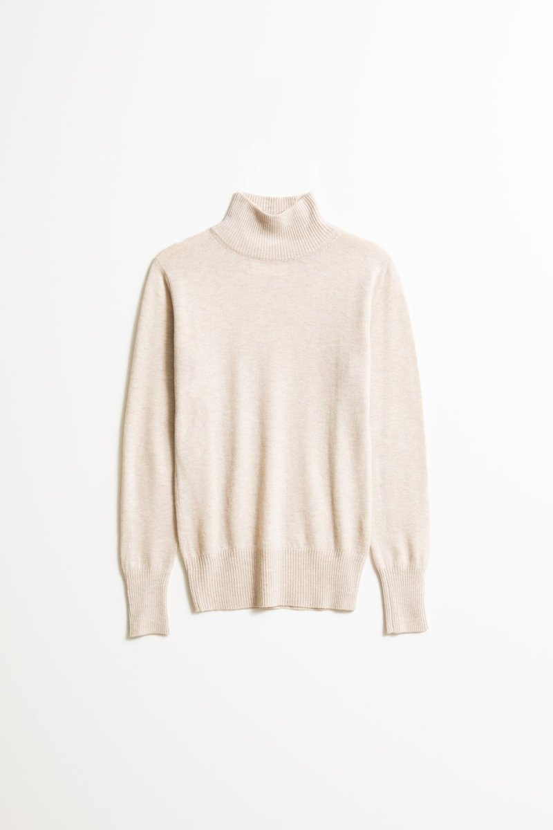 A long sleeve knitted mock neck turtleneck in a cream color. The Merino Turtleneck in Almond White is designed by Dinadi and hand knitted in Kathmandu, Nepal.