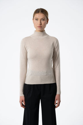 A long sleeve knitted mock neck turtleneck in a cream color. The Merino Turtleneck in Almond White is designed by Dinadi and hand knitted in Kathmandu, Nepal.