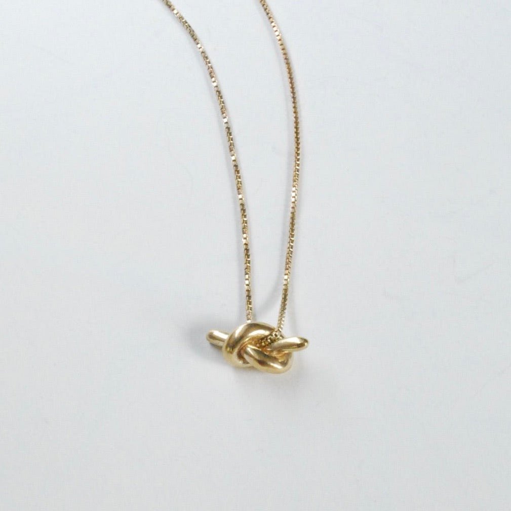 A gold chain necklace with a cast knot design in brass. Then Mini Knot Necklace is designed and handcrafted by Take Shape Studio in Berkeley, California. 