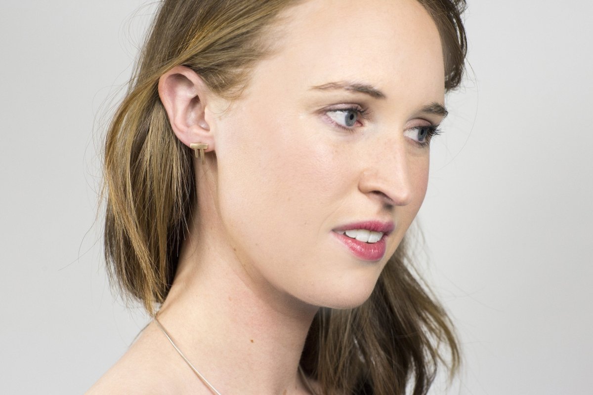 The t-shaped betsy & iya Vous et Moi bronze stud, pictured on the profile of a model with long, straight hair tucked behind her ear.