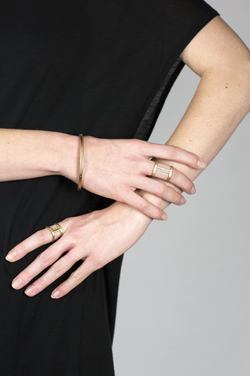 One betsy & iya bronze Juntos bangle, styled on a model with a black tunic, a short betsy & iya Nous ring, and a long betsy & iya Nous ring.