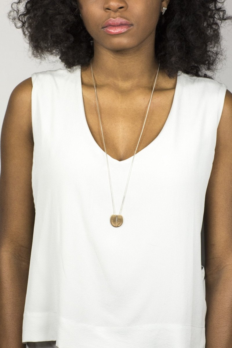 The long version of the cast-bronze and sterling silver Ayni necklace, worn by a model with a white tank top.