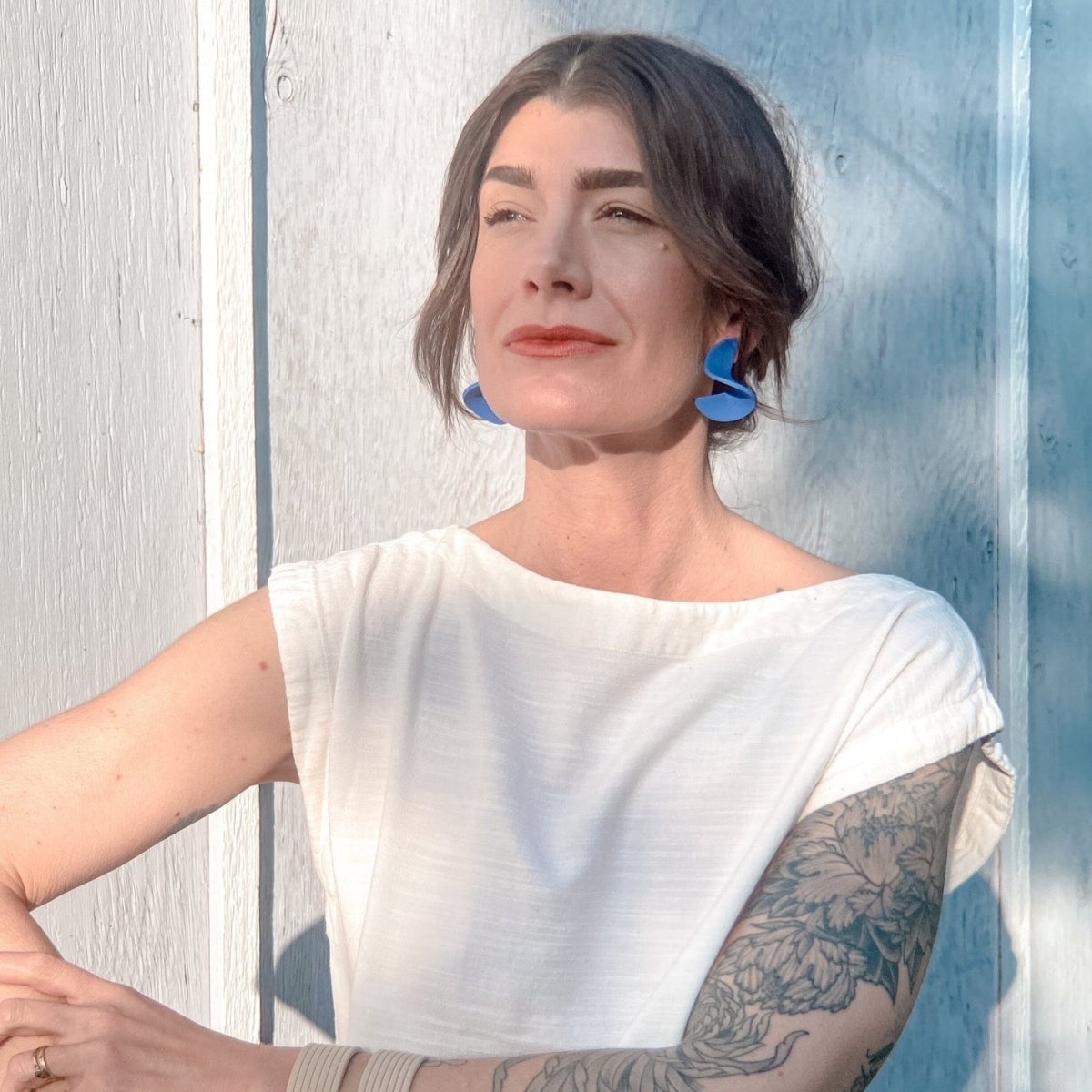 A model wears a polymer clay stud earring folded into a small wave. The Modern Crinkle Earrings in Blue are designed and handcrafted by Little Pieces Jewelry in Los Angeles, California.
