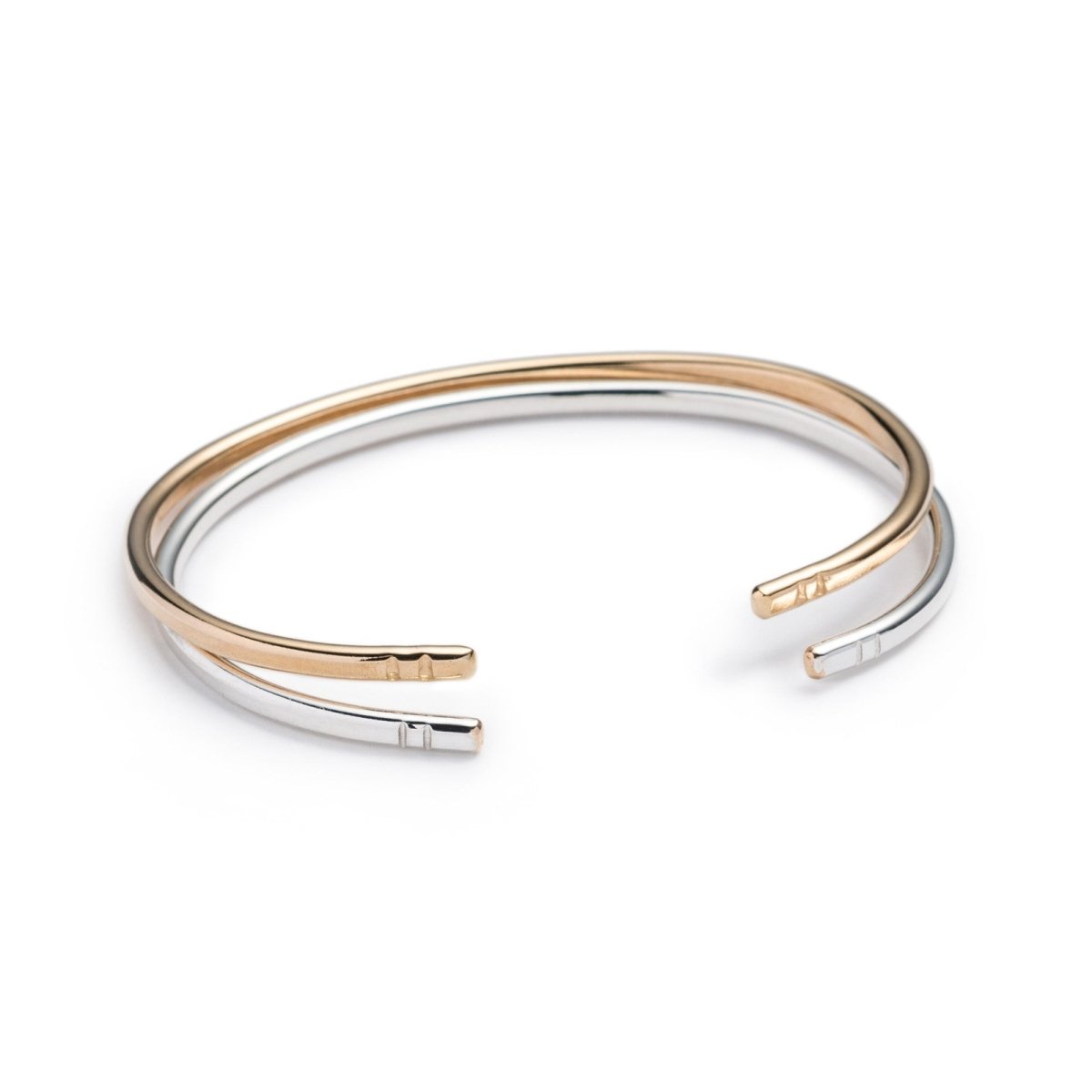 A pair of classic, simple, and adjustable stacking cuffs of hand-forged brass and silver-filled wire, with etched notch details on the ends of the cuffs. Hand-crafted in Portland, Oregon.