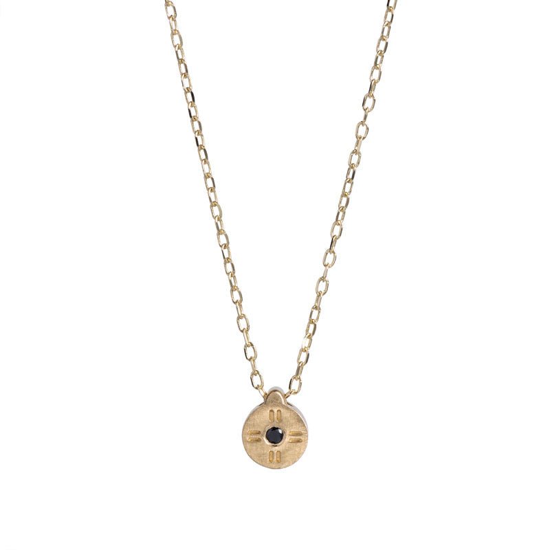 Tiny, circular pendant of 14k yellow gold, with subtle engraved details around a small black diamond, on a 14k gold chain. Hand-crafted in Portland, Oregon.