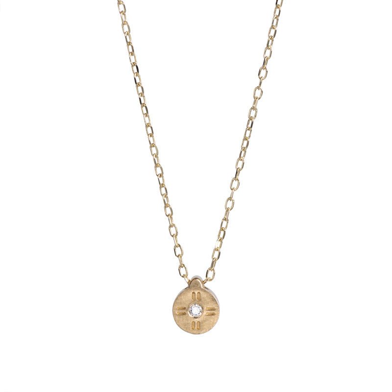 Tiny, circular pendant of 14k yellow gold, with subtle engraved details around a small white diamond, on a 14k gold chain. Hand-crafted in Portland, Oregon. 