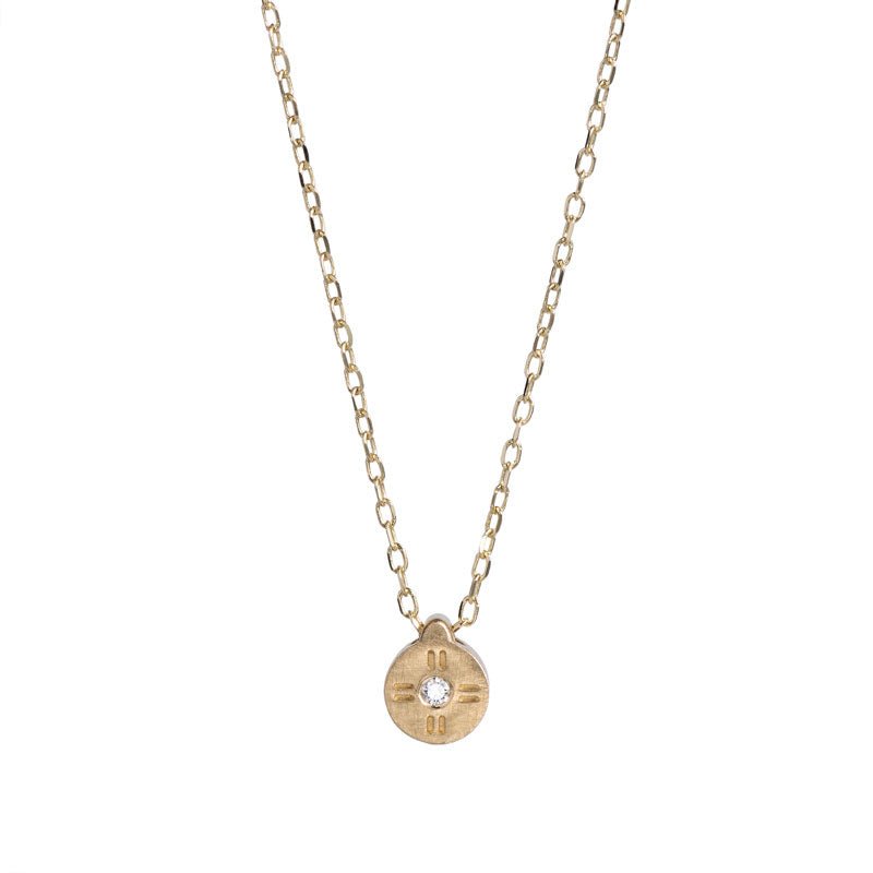 Tiny, circular pendant of 14k yellow gold, with subtle engraved details around a small white diamond, on a 14k gold chain. Hand-crafted in Portland, Oregon.