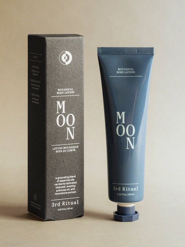 A blue tube of lotion stands next to a grey rectangular box. The Moon Botanical Body Lotion is developed and formulated by 3rd Ritual in New York City, NY.
