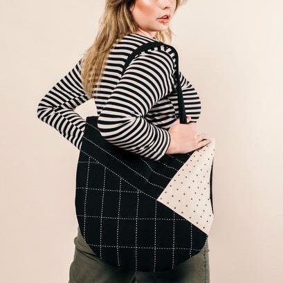 Model wears black tote with white cross-stitching and color-blocked design. Designed by Anchal in Louisville, Kentucky and handmade in Ajmer, India.