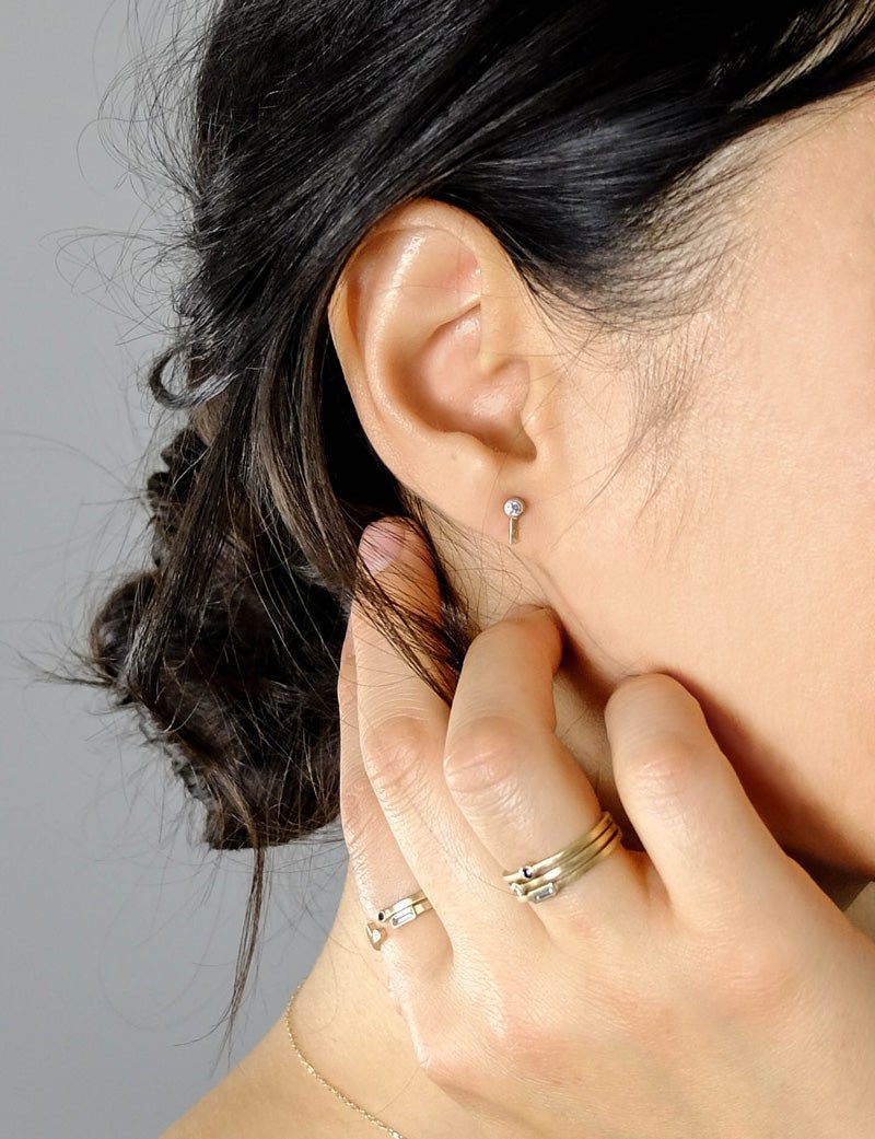 14k yellow gold and white diamond Navitas stud earrings by betsy & iya, pictured on a model with dark hair and stacks of betsy & iya Nitor, Robur, and Manus rings.