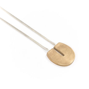 Circular, cast-bronze pendant with a flat top and rectangular cutout that starts at the top and runs halfway through the center of the circle, threaded through the back of the pendant with a sterling silver snake chain. Hand-crafted in Portland, Oregon. 