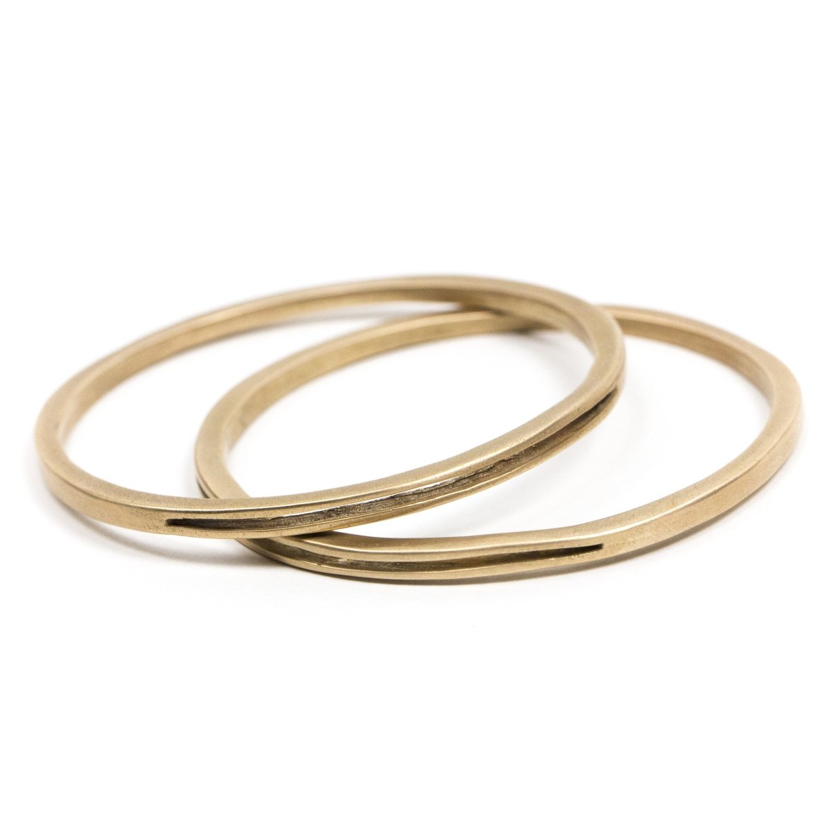 A pair of sturdy, circular, cast-bronze bangle bracelets, each with one long, slim, cutout slit in the metal. Hand-crafted in Portland, Oregon.
