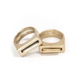 A set of silver and cast bronze Tuyo and Mía rings, propped up against the edge of a set of all-bronze Tuyo and Mía rings. Hand-crafted in Portland, Oregon.