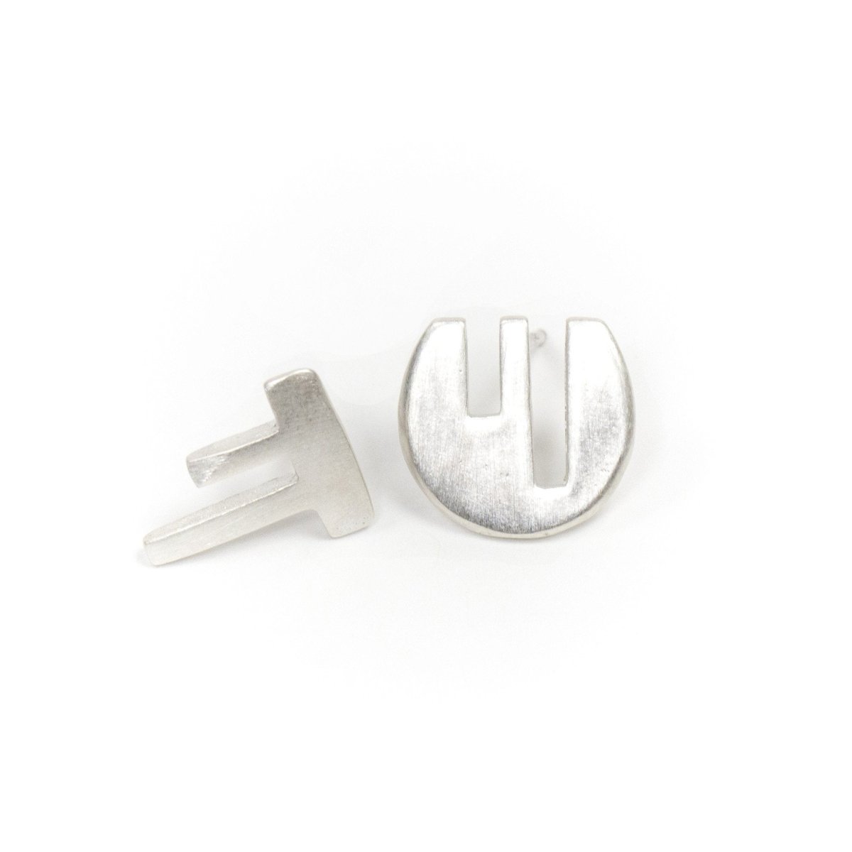 A pair of mismatched, fine silver stud earrings, with complementary geometric cutouts that fit into one another like puzzle pieces. Hand-crafted in Portland, Oregon.