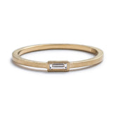 Thin, 14k yellow gold ring with a matte finish and a small, white diamond baguette bezel-set parallel to the band. Hand-crafted in Portland, Oregon.