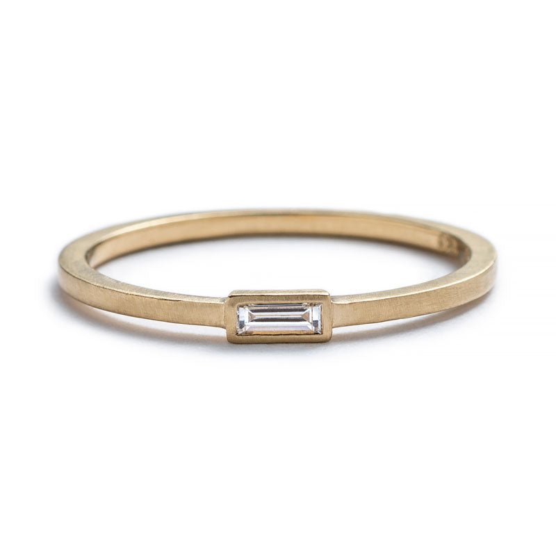 Thin, 14k yellow gold ring with a matte finish and a small, white diamond baguette bezel-set parallel to the band. Hand-crafted in Portland, Oregon.